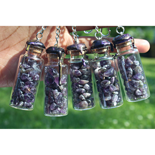 Obsidian, rose quartz, and amethyst crystals inside clear glass jar with wax seals and keychain attachments by gravely goods in a hand outside