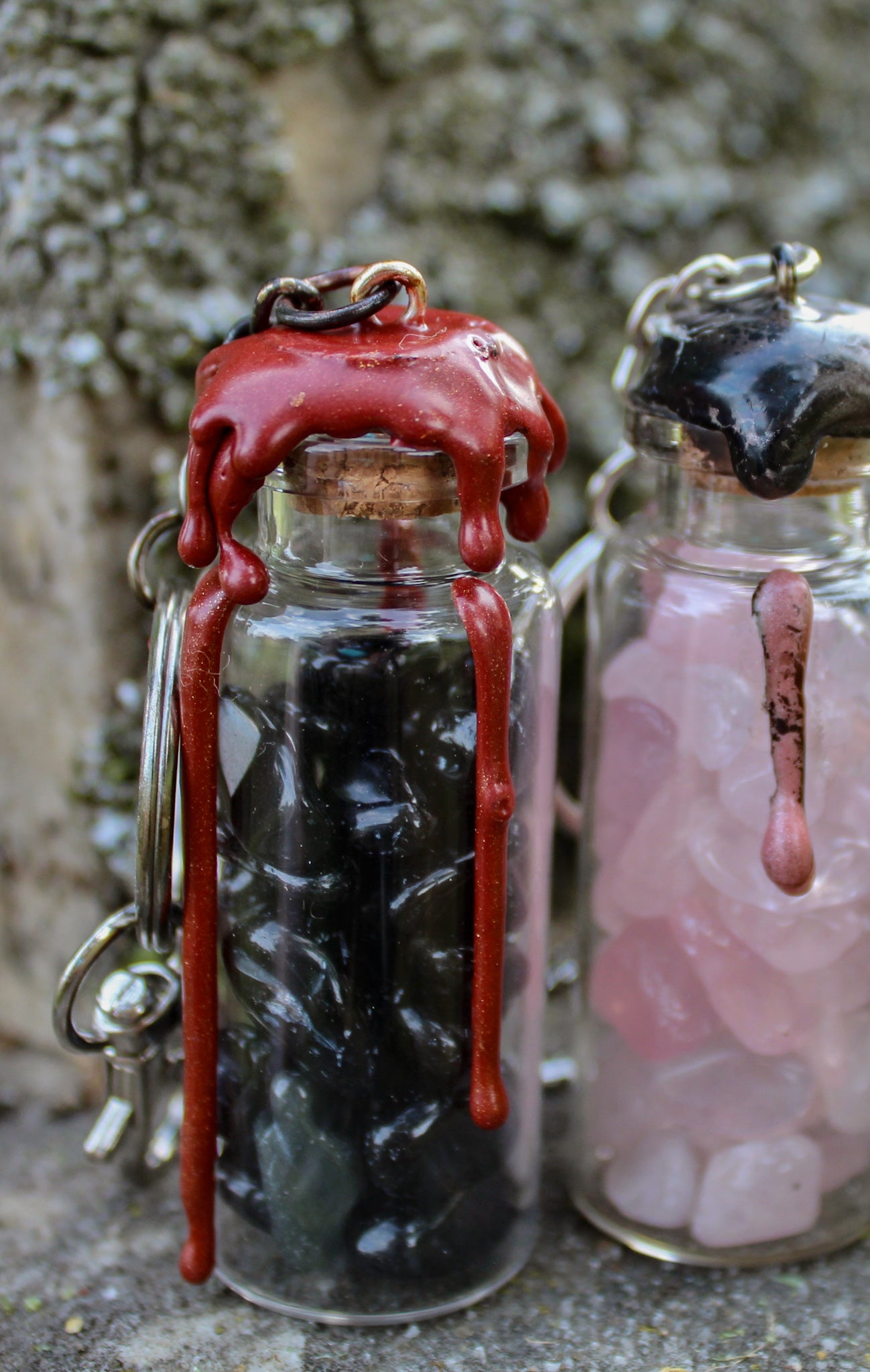 Obsidian, rose quartz crystals inside clear glass jar with wax seals and keychain attachments in front of an old tombstone