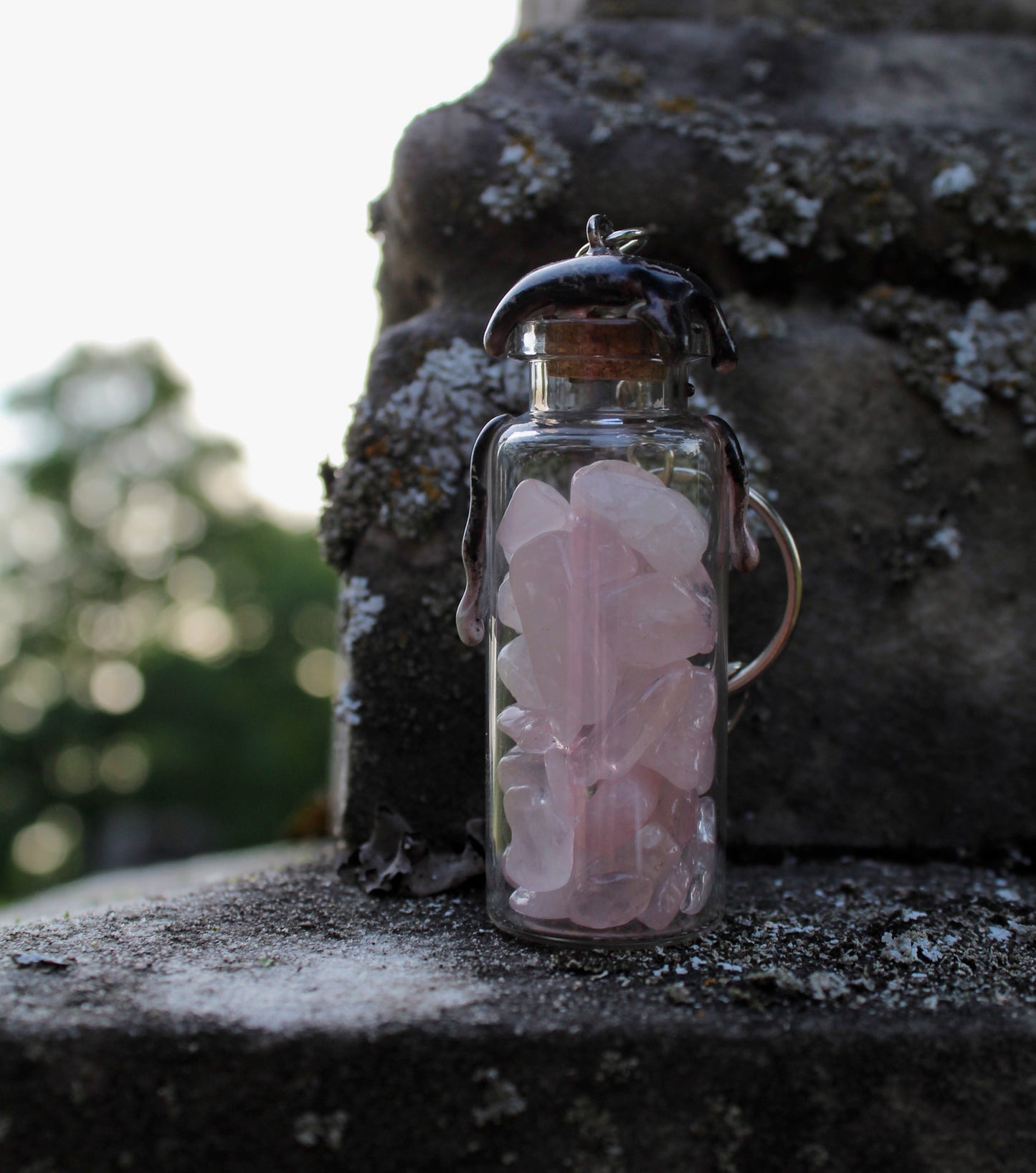 Obsidian, rose quartz, and amethyst crystals inside clear glass jar with wax seals and keychain attachments in front of an old tombstone