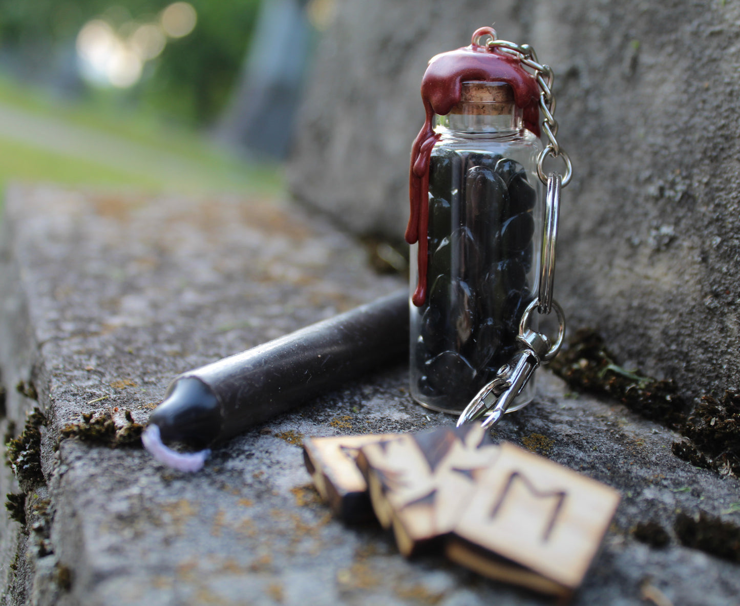 Obsidian, rose quartz, and amethyst crystals inside clear glass jar with wax seals and keychain attachments in front of an old tombstone with black spell candle and wood carved runes by gravely goods