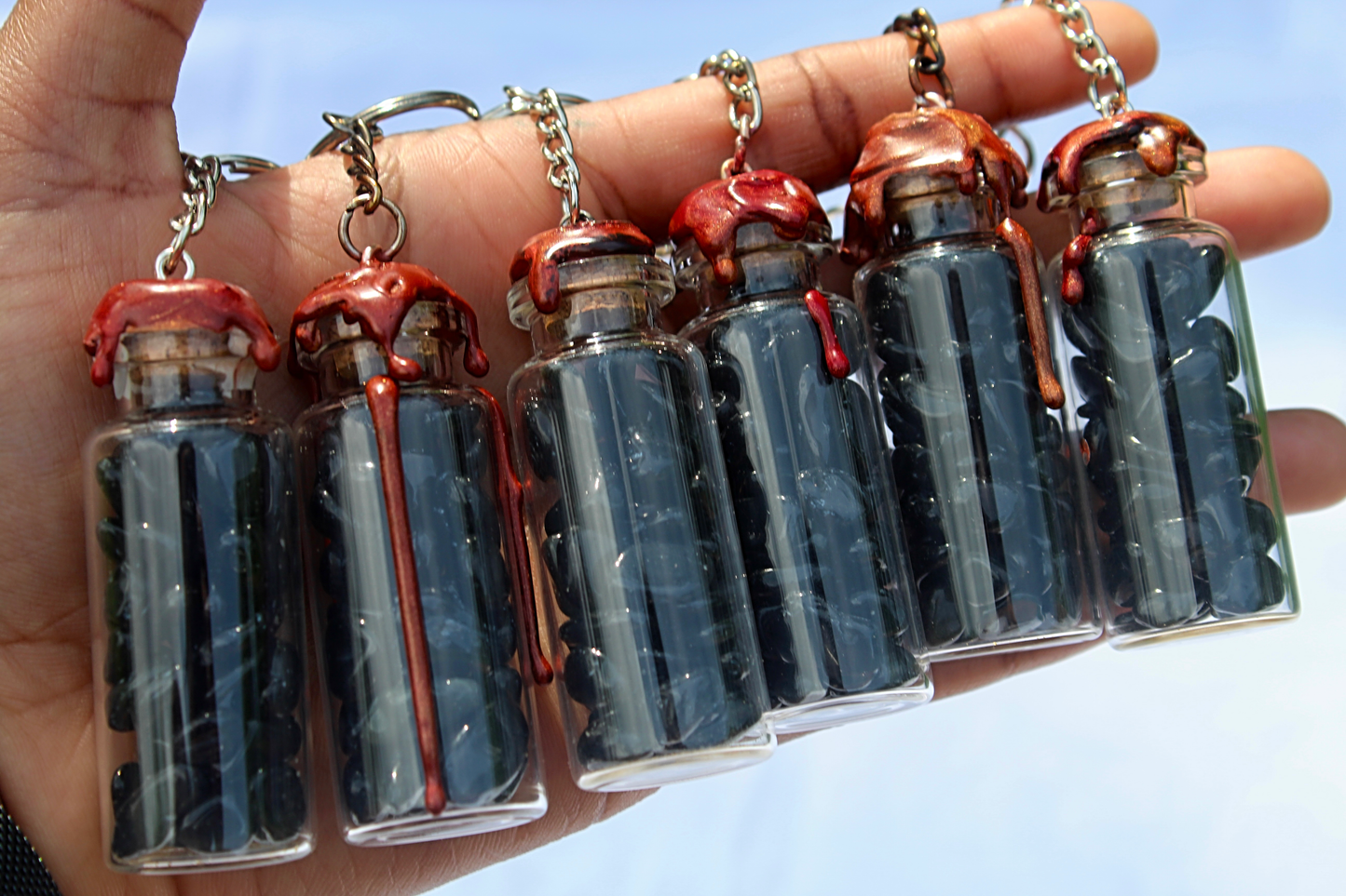 Obsidian, rose quartz, and amethyst crystals inside clear glass jar with wax seals and keychain attachments by gravely goods in a hand outside
